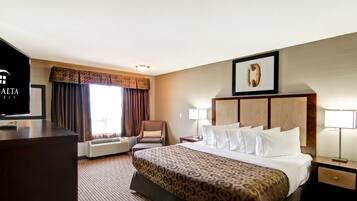 A hotel room with a large bed, a desk, a chair, a TV, and a framed picture on the wall.