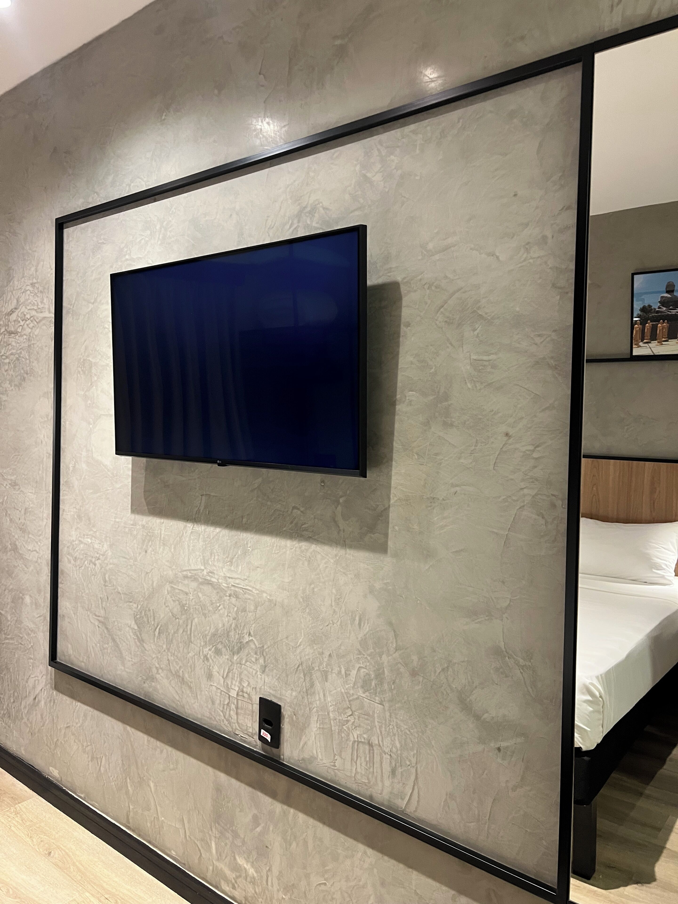 Una habitación moderna con un televisor de pantalla plana montado en una pared texturizada, un cabecero de madera y una mesita de noche pequeña.
