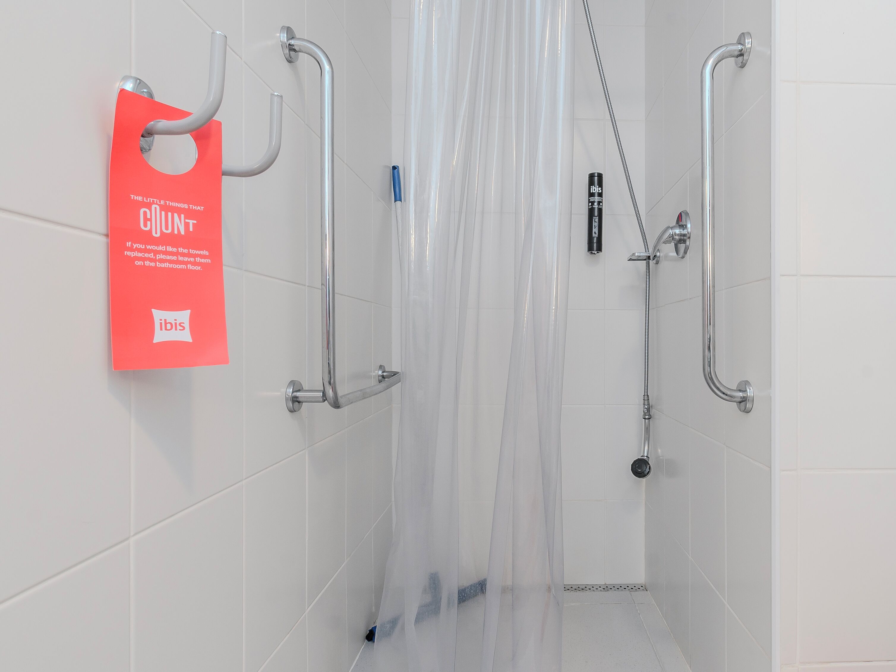 A shower with a transparent curtain, a handheld showerhead, and a handheld soap dispenser.