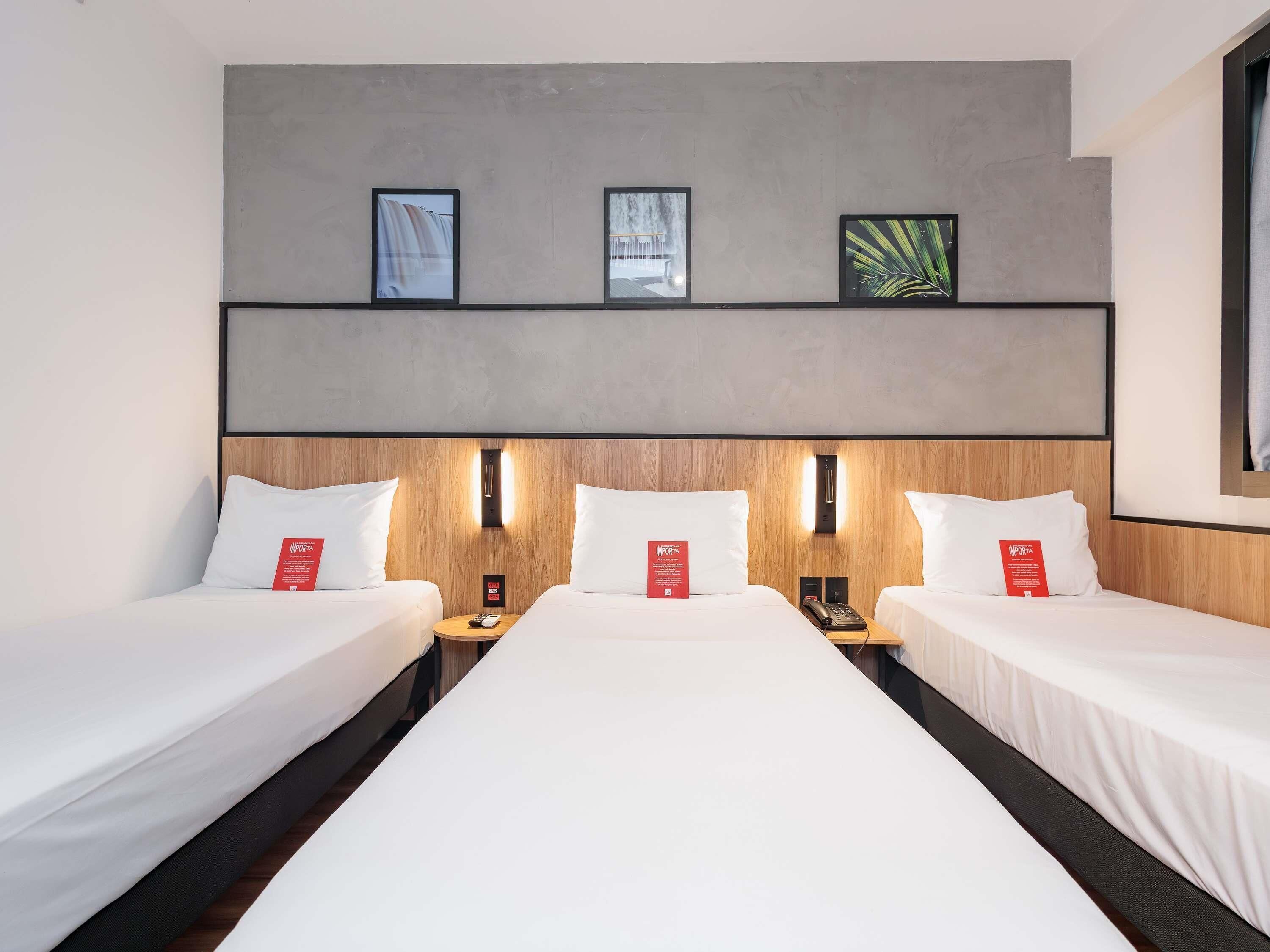A hotel room with two beds, a wooden headboard, and three framed pictures on the wall.