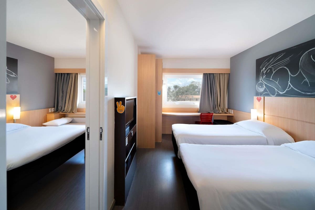 A hotel room with two beds, a TV, a window with curtains, and a painting on the wall.