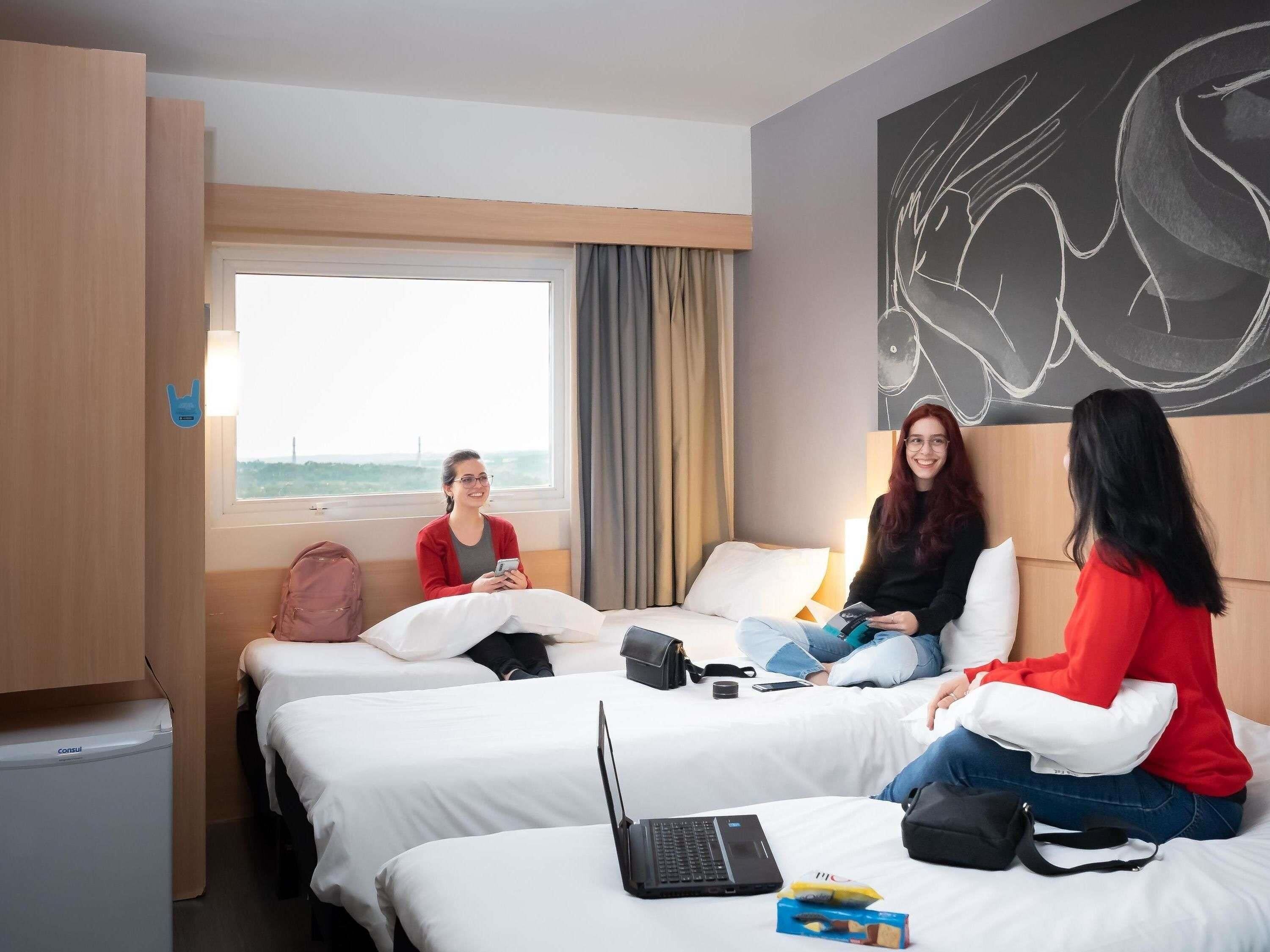 Une chambre d’hôtel avec deux lits, un ordinateur portable, un sac à dos et une fenêtre donnant sur un beau paysage.