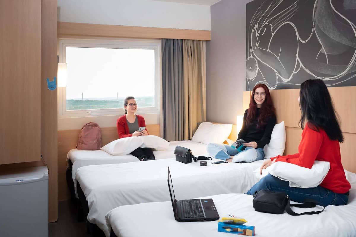 A hotel room with two beds, a window with a view, a laptop on one bed, and a backpack on the floor.