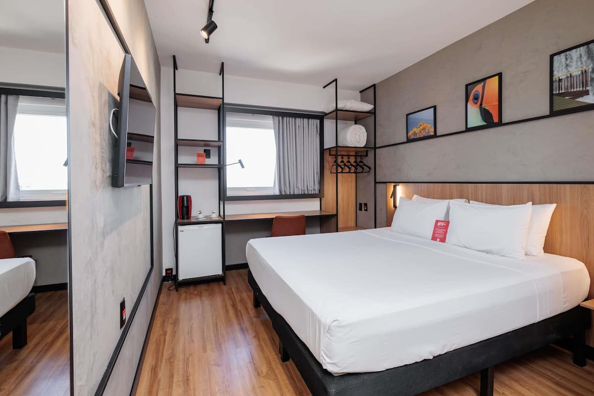 A modern hotel room with a bed, desk, and wardrobe.
