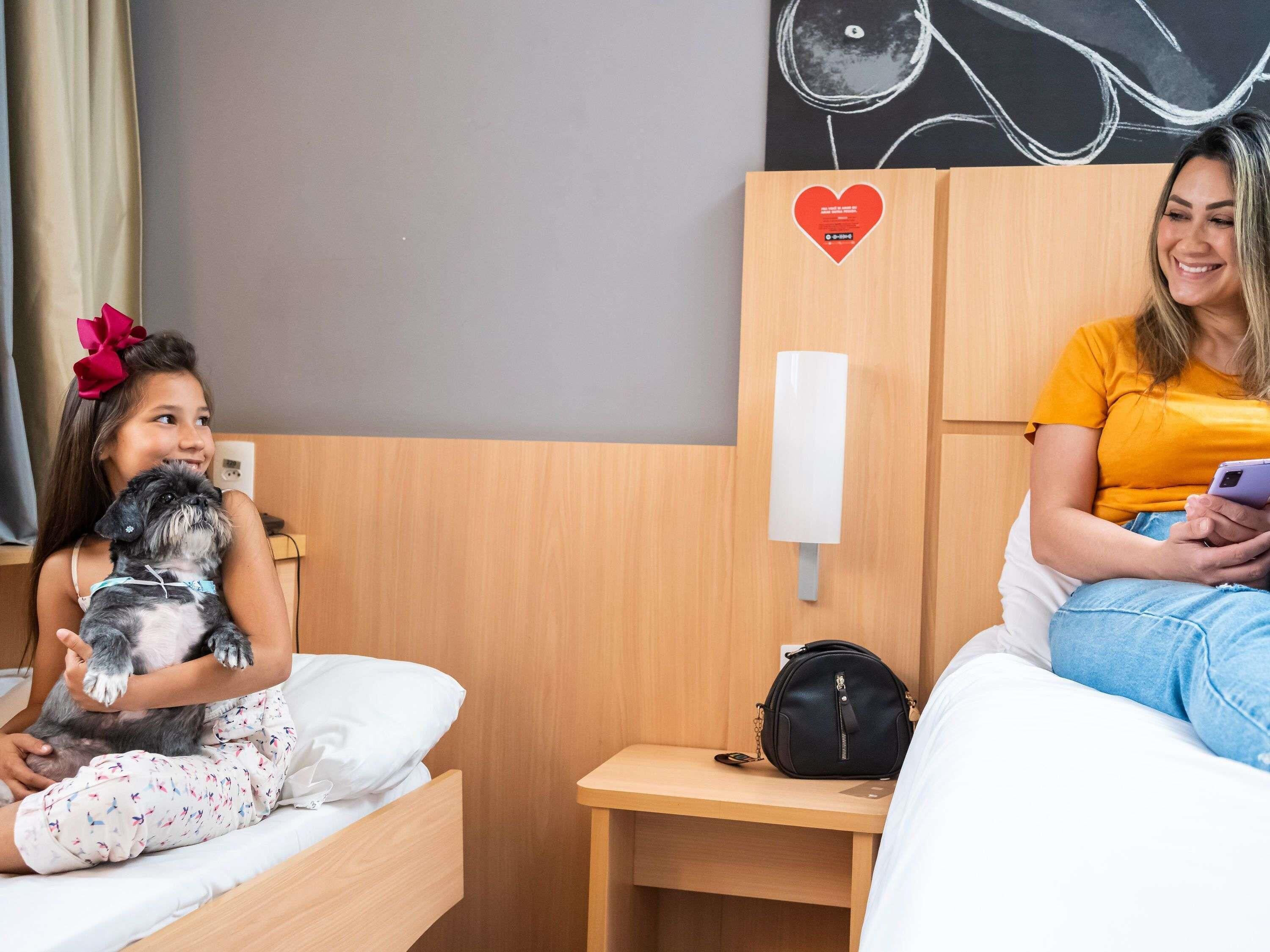 Ein Hotelzimmer mit zwei Betten, einem Nachttisch, einem an der Wand befestigten Telefon und einer kleinen Wanddekoration.