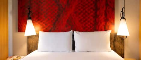 A hotel room with a large bed, two bedside tables, a red textured wall, and two pendant lights.
