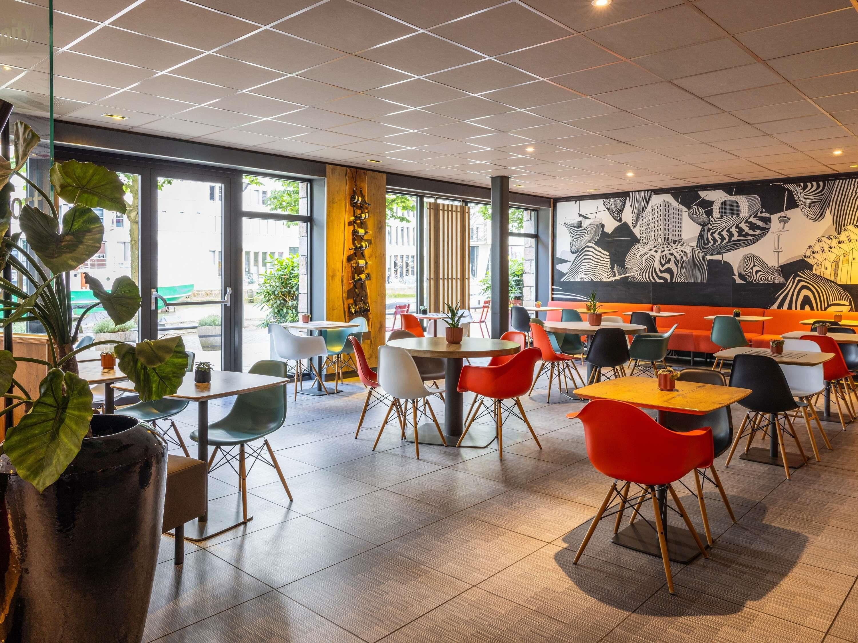 A modern cafe interior with a mix of seating arrangements, including tables and booths, and a large mural on the wall.