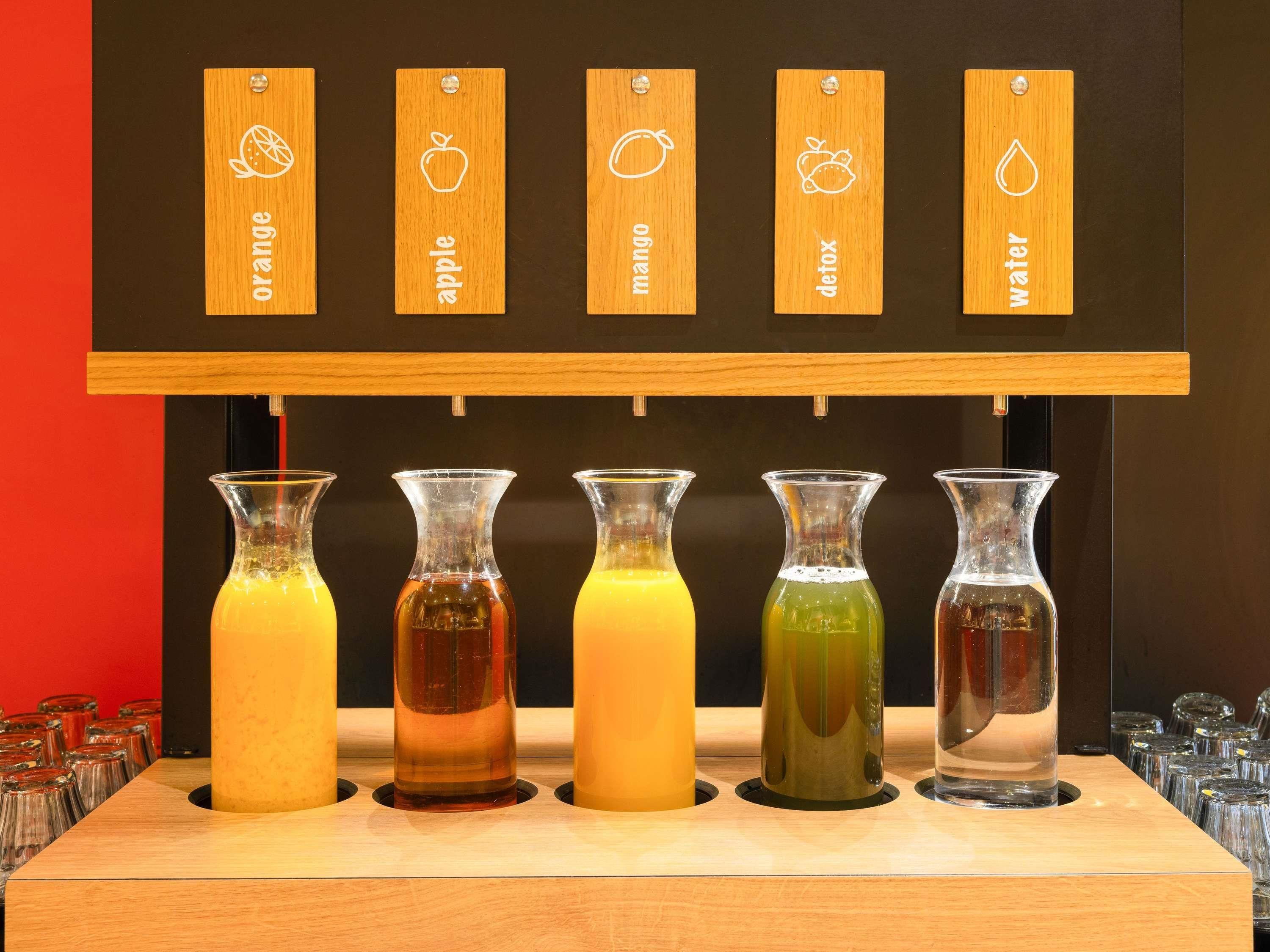 Un bar proposant des boissons aux saveurs d’orange, de pomme, de mangue, détox et d’eau, avec des étiquettes en bois indiquant les différents parfums.