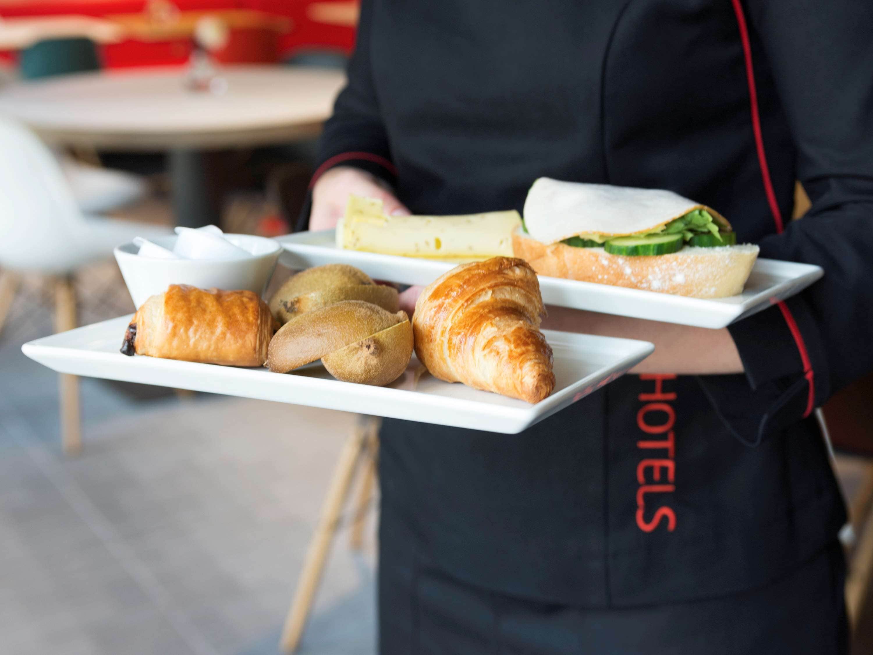 A person holding a tray with croissants, a sandwich, and a bowl of soup.