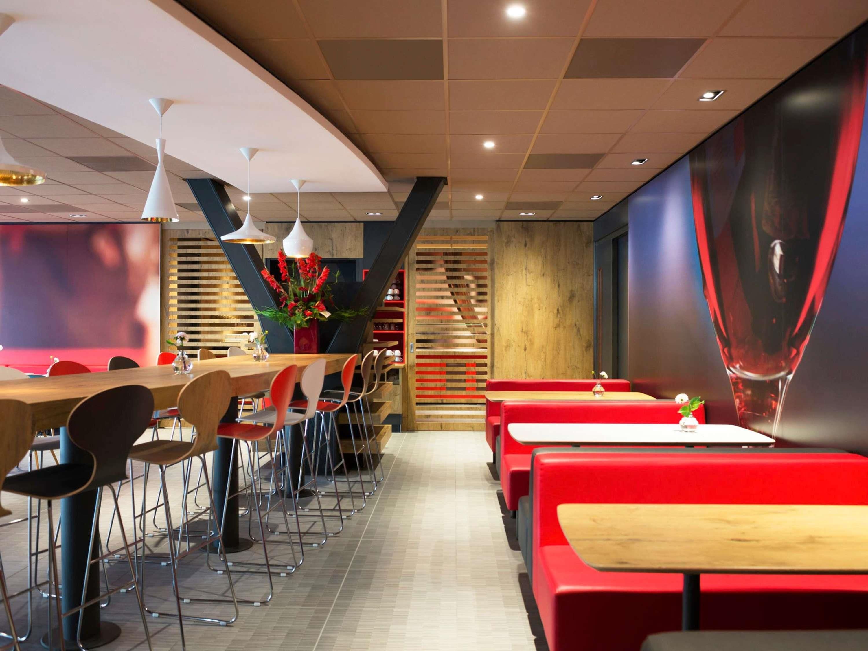 A modern restaurant interior with wooden tables and red booths, a large screen, and a staircase.