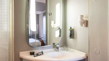 A hotel bathroom with a large mirror, a sink, and toiletries.