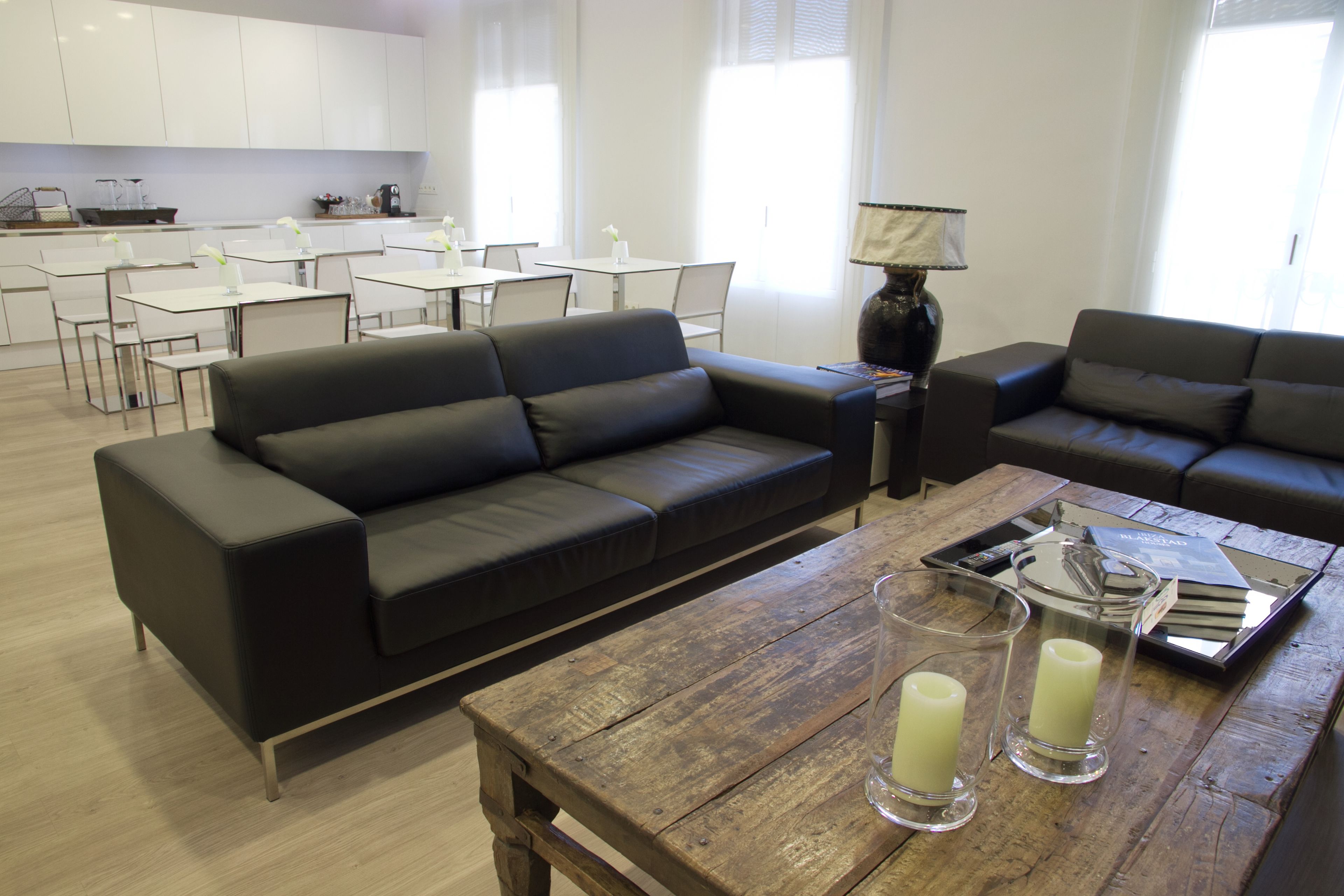 A modern living room with a black leather sofa, a wooden coffee table, and a dining area with white tables and chairs.