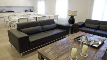 A modern living room with a black leather sofa, a wooden coffee table, and a dining area with white tables and chairs.