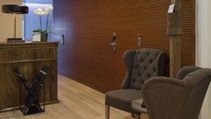 A reception area with a wooden reception desk, a grey upholstered chair, and a potted orchid. - THE 8 Boutique B&B (Barcelona)