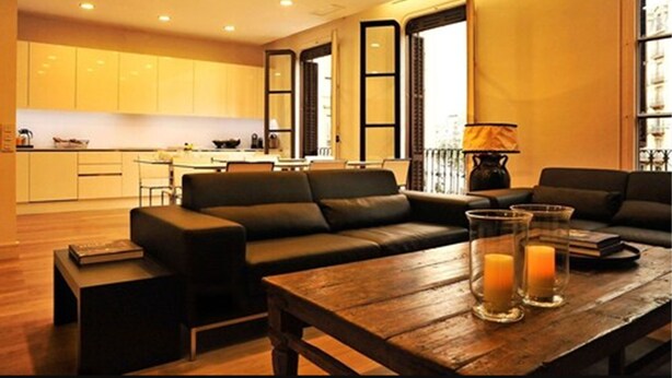 A modern living room with a sofa, a wooden coffee table with candles, and a kitchen in the background. - THE 8 Boutique B&B (Barcelona)