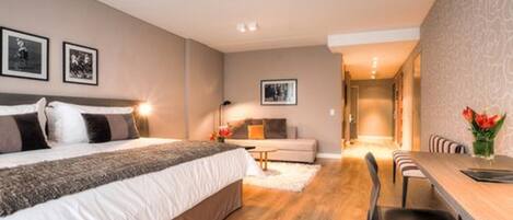Une chambre moderne avec un grand lit, un canapé, une table à manger avec des chaises et un couloir menant à une autre pièce.
