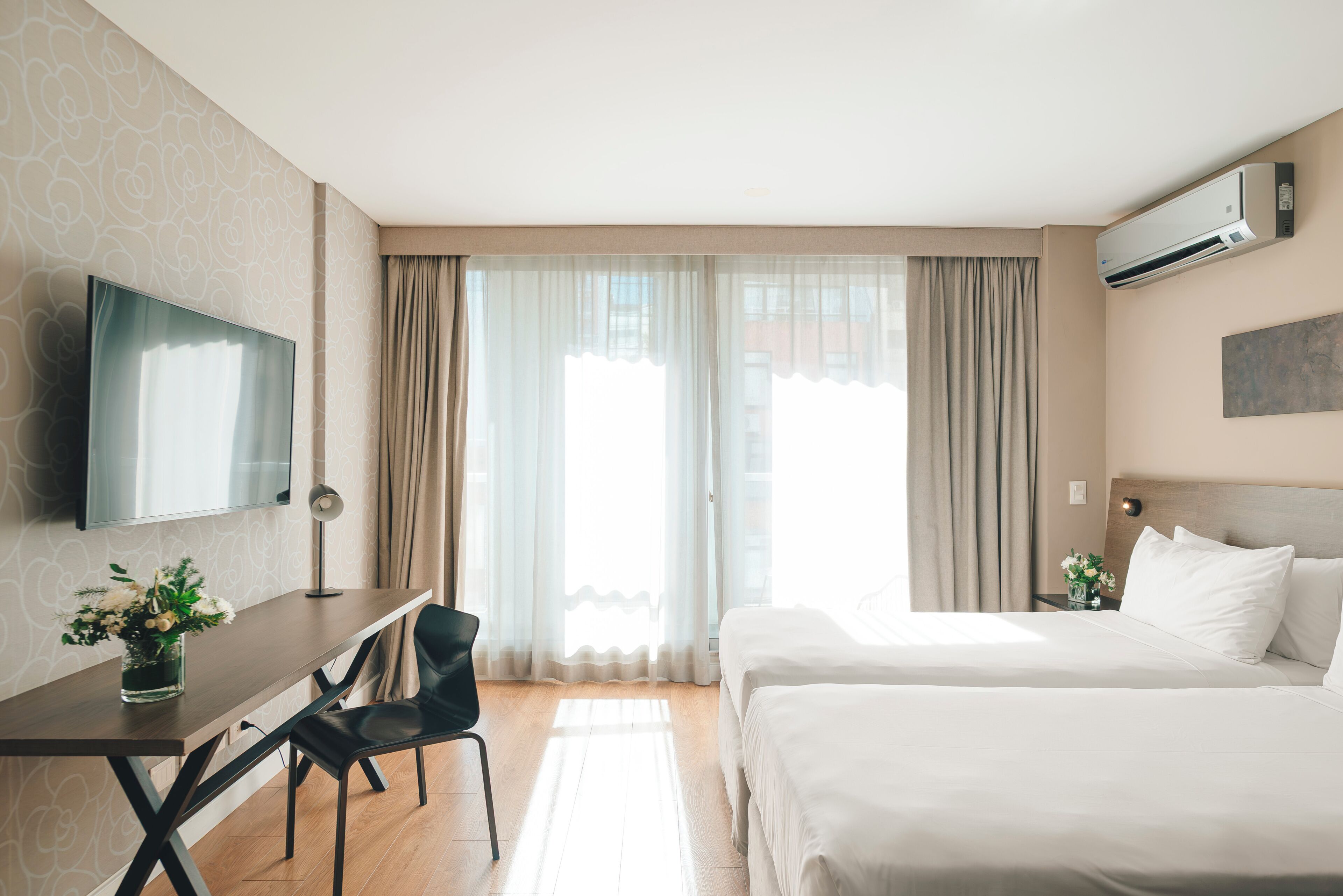 Et hotelværelse med seng, skrivebord, stol, fjernsyn og et vindue med gardiner.