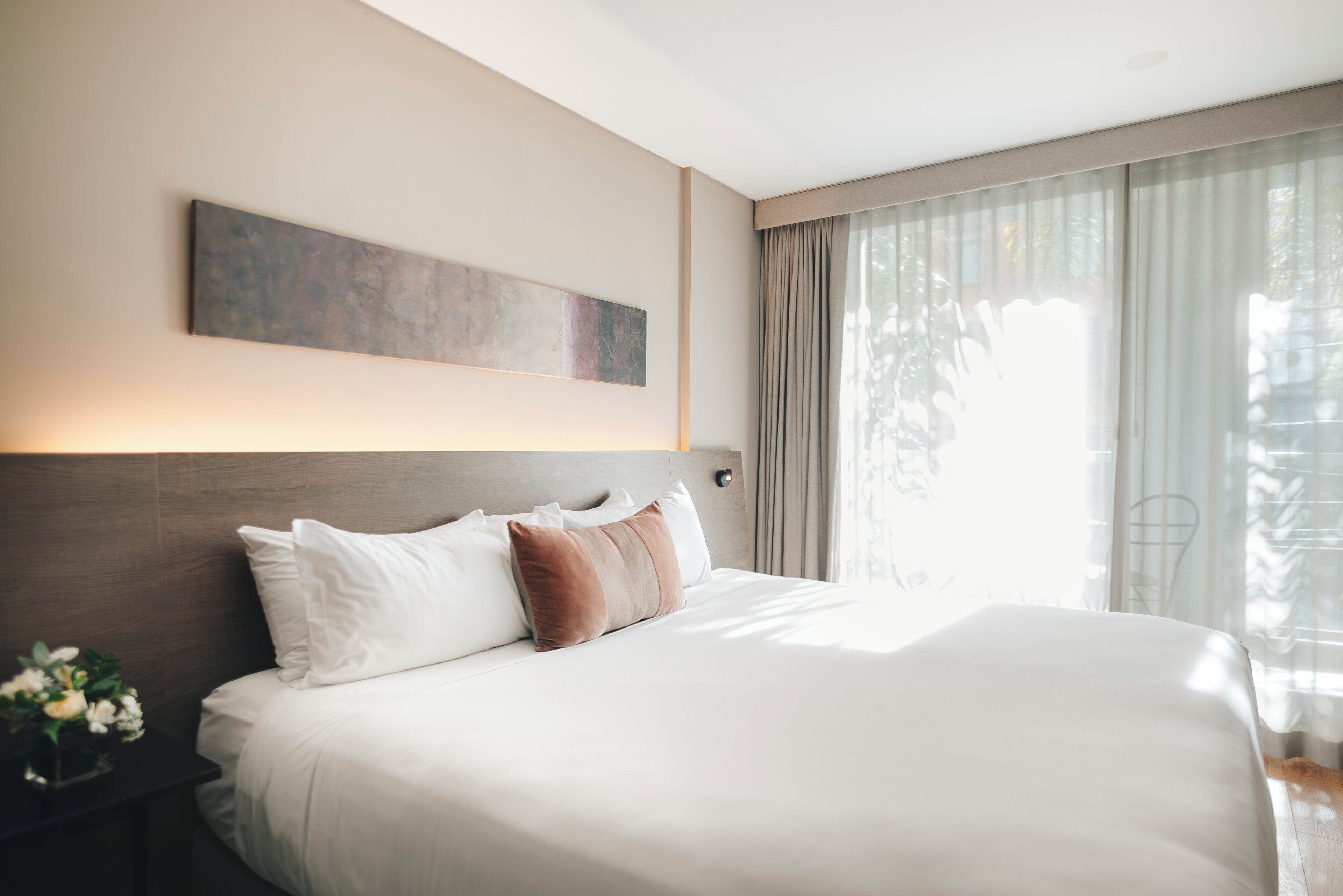 A hotel room with a large bed, a headboard, a wall-mounted artwork, and a window with curtains.