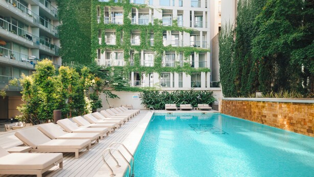 A swimming pool with lounge chairs, surrounded by a building with greenery and a tiled deck. - CasaSur Bellini (Buenos Aires)