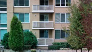 A rectangular pool with clear blue water, surrounded by a low concrete edge and bordered by a grassy area with small bushes and a tree. - Crystal Quarters Furnished Apartments- Concord (Arlington)