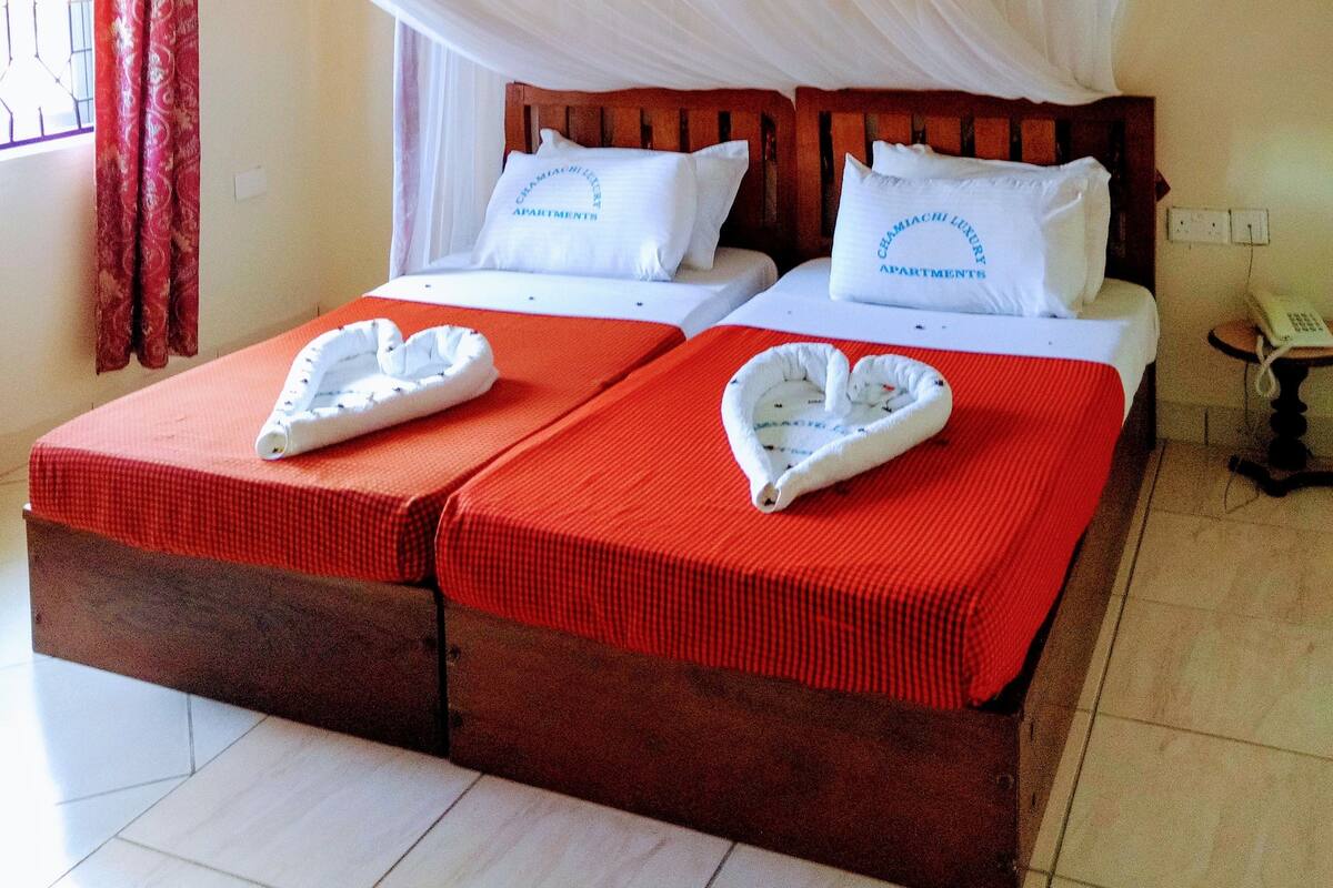 A double bed with a red bedspread and two pillows, a wooden headboard, and a white canopy.