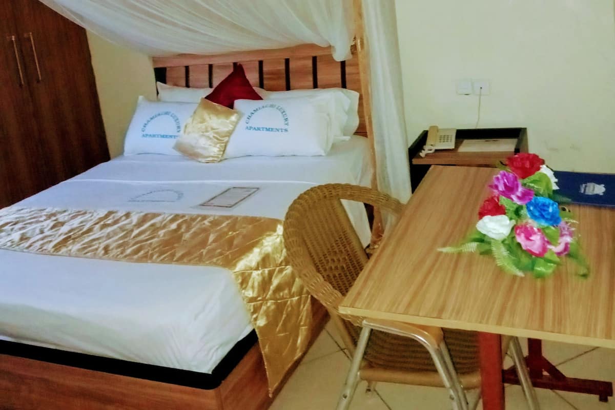 A bed with a canopy, a bedside table with a vase of flowers, and a wooden chair.