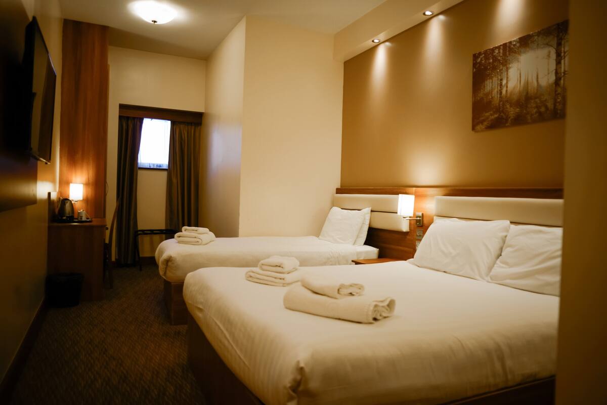 A hotel room with two beds, a TV, a window with curtains, and a painting on the wall.