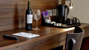 A wooden counter with a bottle of wine, a glass, a coffee maker, and a tray with coffee cups and packets.