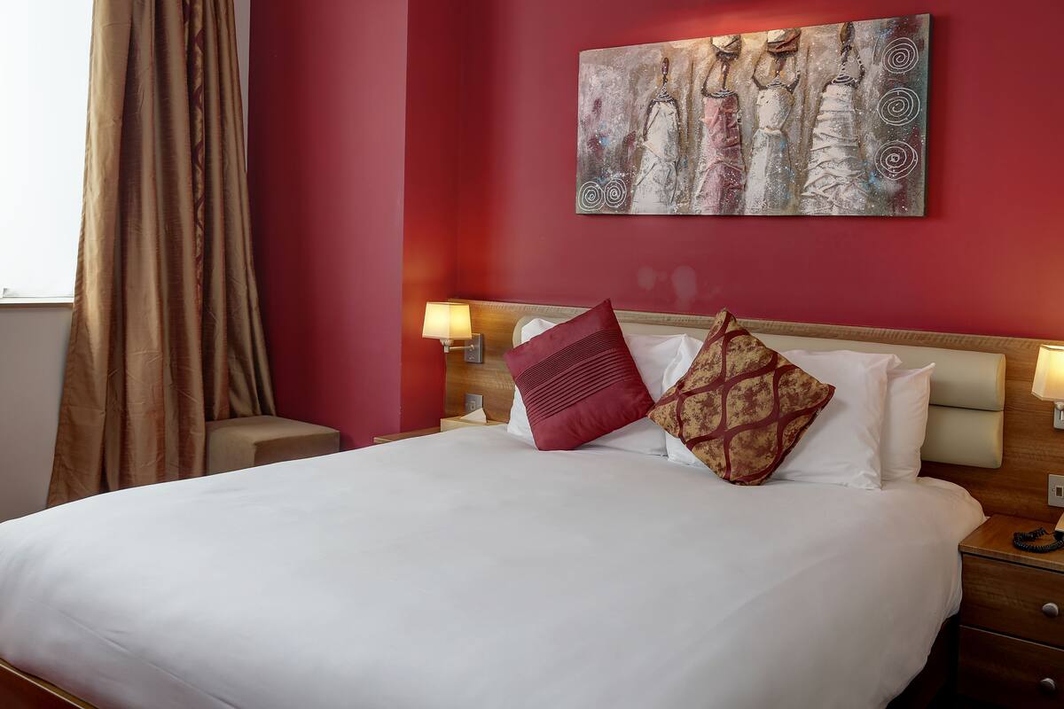 A hotel room with a large bed, red walls, and a painting above the bed.