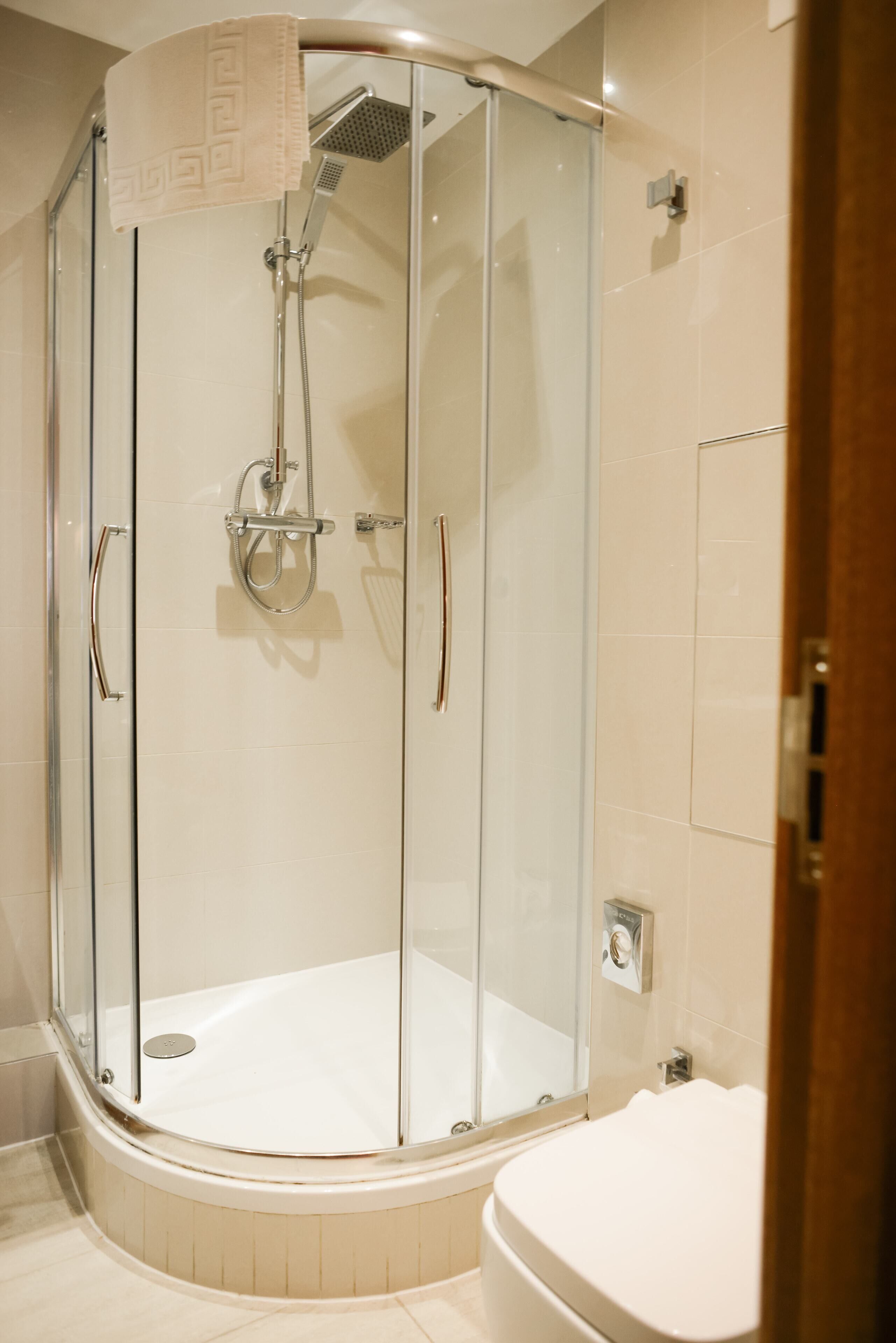 A glass-enclosed shower with a handheld showerhead, a towel, and a toilet visible in a modern bathroom.