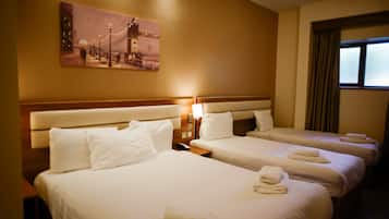 A hotel room with three beds, a painting on the wall, and a window with curtains.
