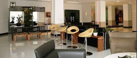 A modern hotel lobby with a reception desk, seating area, and a large flat-screen TV.