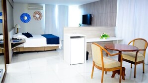 A modern hotel room with a bed, bedside table, lamp, TV, and a small desk with a chair. - Posseidon Hotel (Imperatriz)