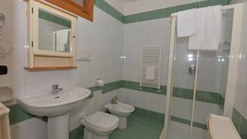 Un baño con lavamanos, dos inodoros, un bidé, un espejo y una ducha con puerta de cristal.