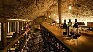 A wine cellar with wooden racks holding wine bottles, a bar area with bottles and glasses, and a stone ceiling. - Ulfsunda Slott (Bromma)