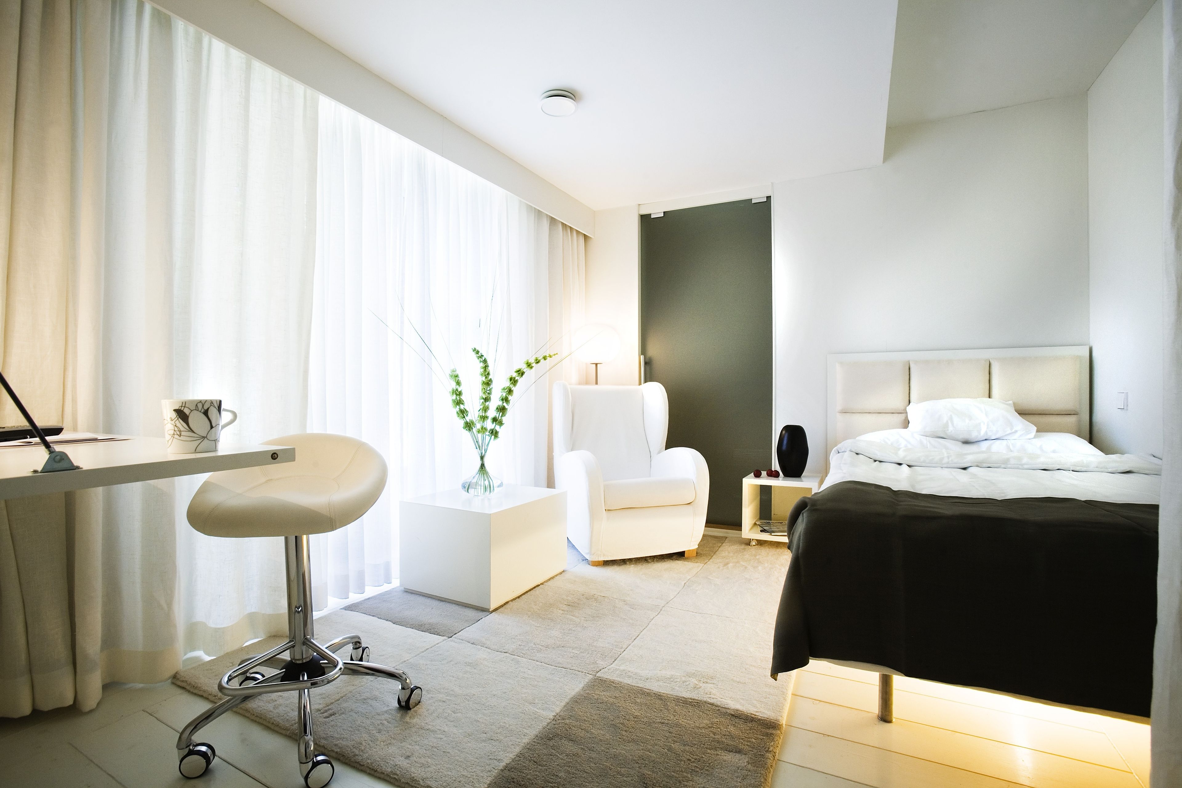Quarto de hotel moderno com uma cama, uma escrivaninha, uma cadeira e uma mesinha.