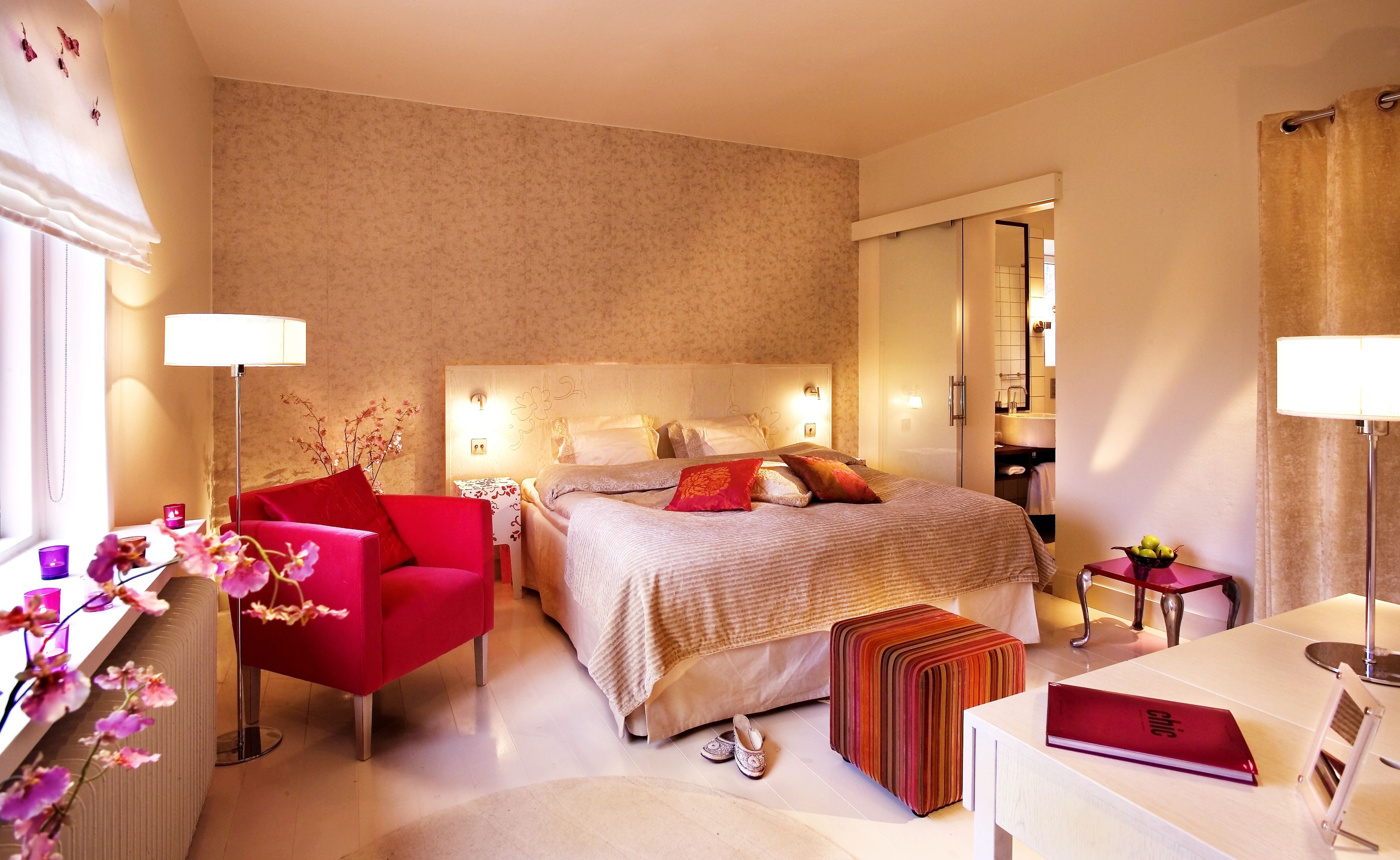 Una habitación de hotel con una cama, una silla roja, una mesita y una mesita de noche.