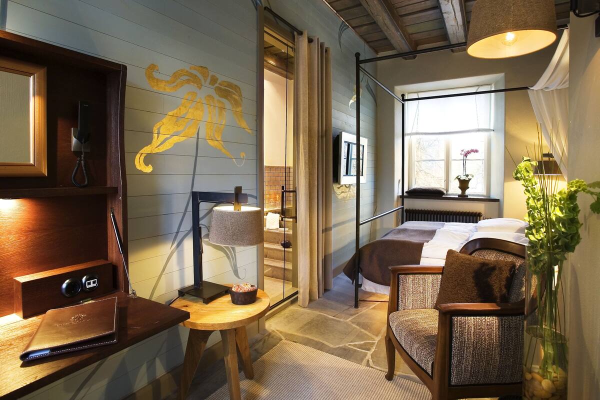 A cozy room with a bed, a chair, a desk with a lamp, and a wall with a yellow design.