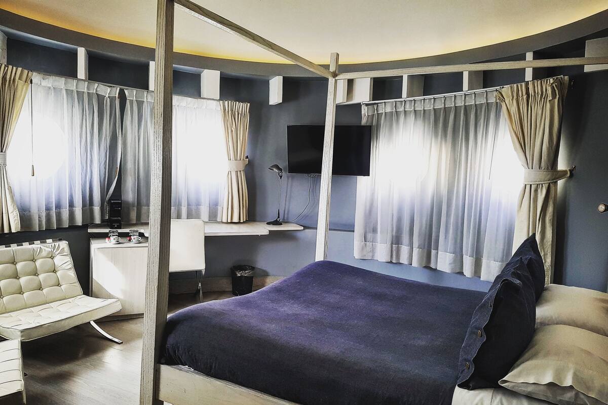 A bedroom with a bed, a desk, a chair, and curtains.
