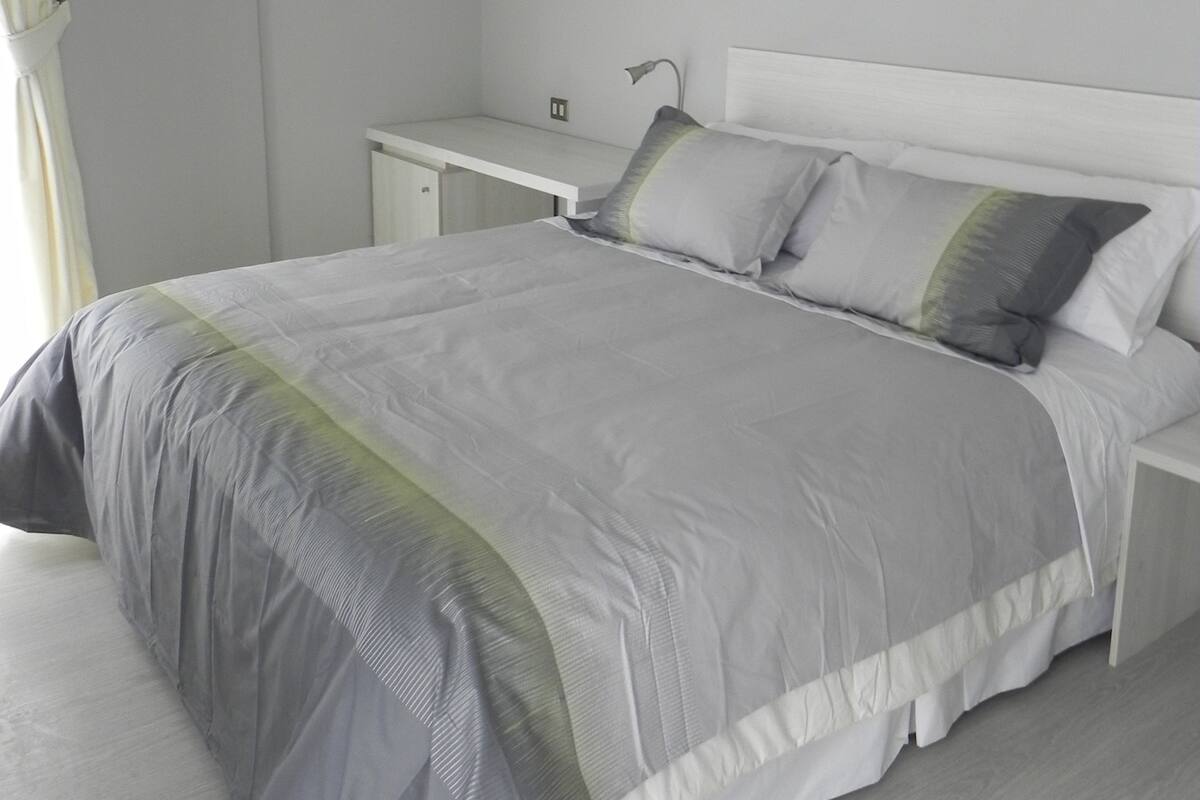 A modern bedroom with a large bed, bedside tables, and a hanging light fixture.