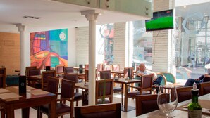A restaurant interior with wooden tables and chairs, a large TV screen, and a colorful mural on the wall. - Hotel Terranostra (Valparaiso)