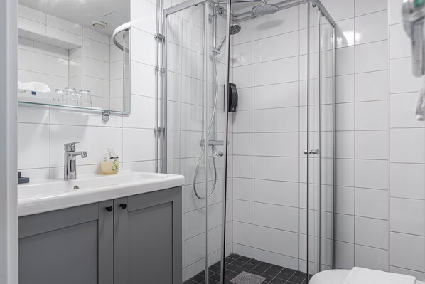 Un baño moderno con ducha de vidrio, un lavabo blanco con dispensador de jabón y un espejo sobre el lavabo.