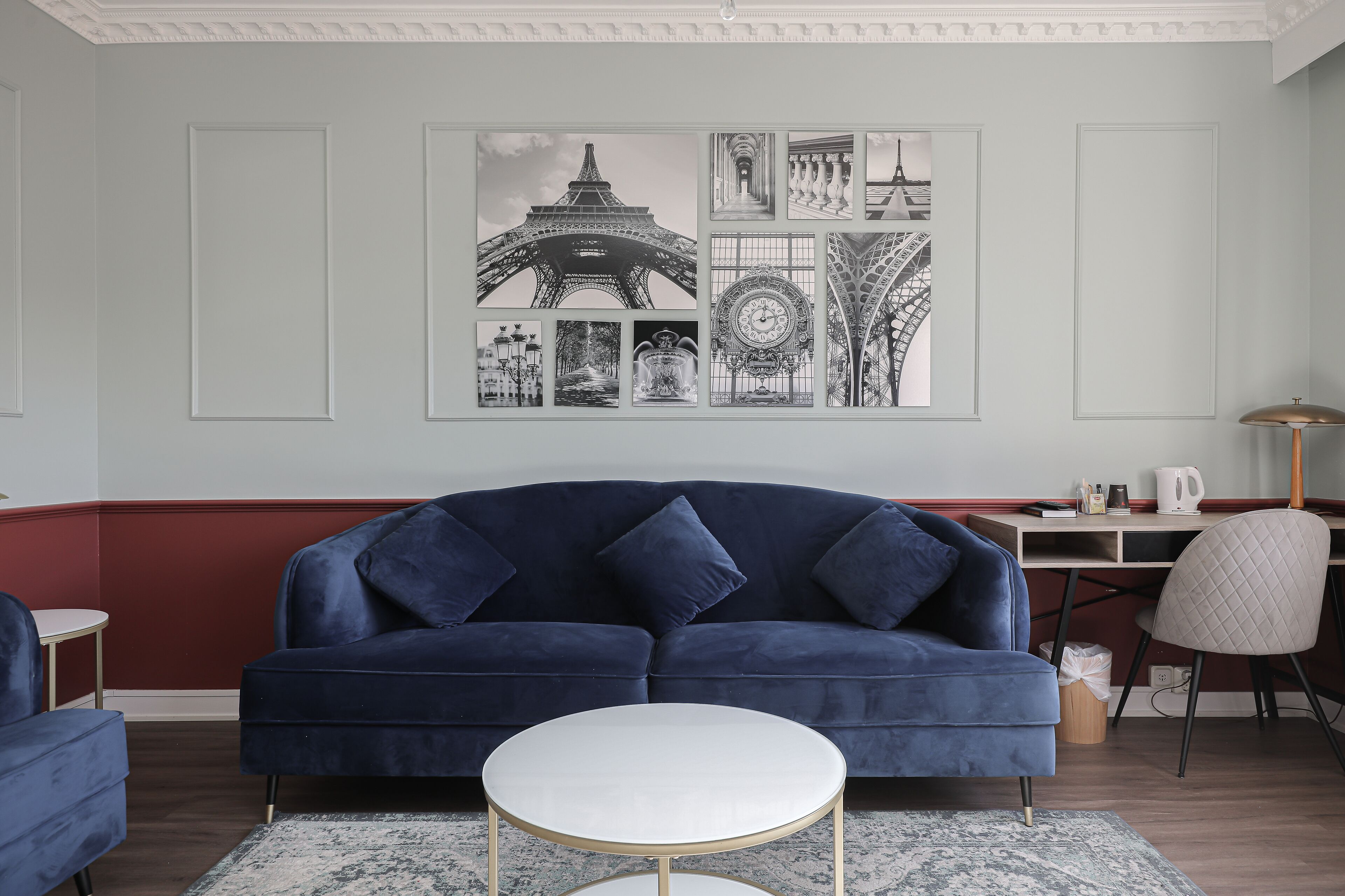 Un salón con un sofá azul oscuro, una mesa de centro blanca y una pared decorada con fotografías en blanco y negro de monumentos parisinos.