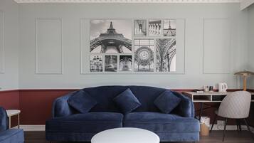 Un salón con un sofá azul oscuro, una mesa de centro blanca y una pared decorada con fotografías en blanco y negro de monumentos parisinos.