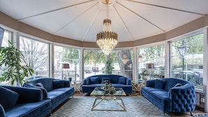 A spacious room with a large bay window, a chandelier, and a blue sofa set. - Hotell Arkad (Vasteras)