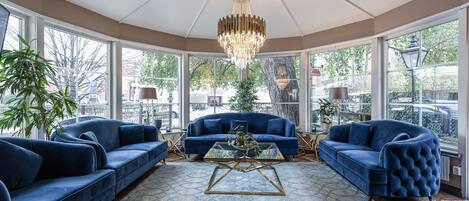 A spacious room with a large bay window, a chandelier, and a blue sofa set.
