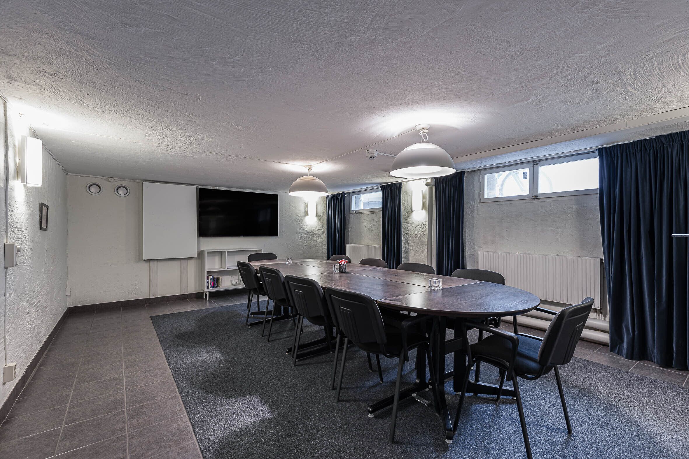 A conference room with a large table, black chairs, a whiteboard, and a TV screen.