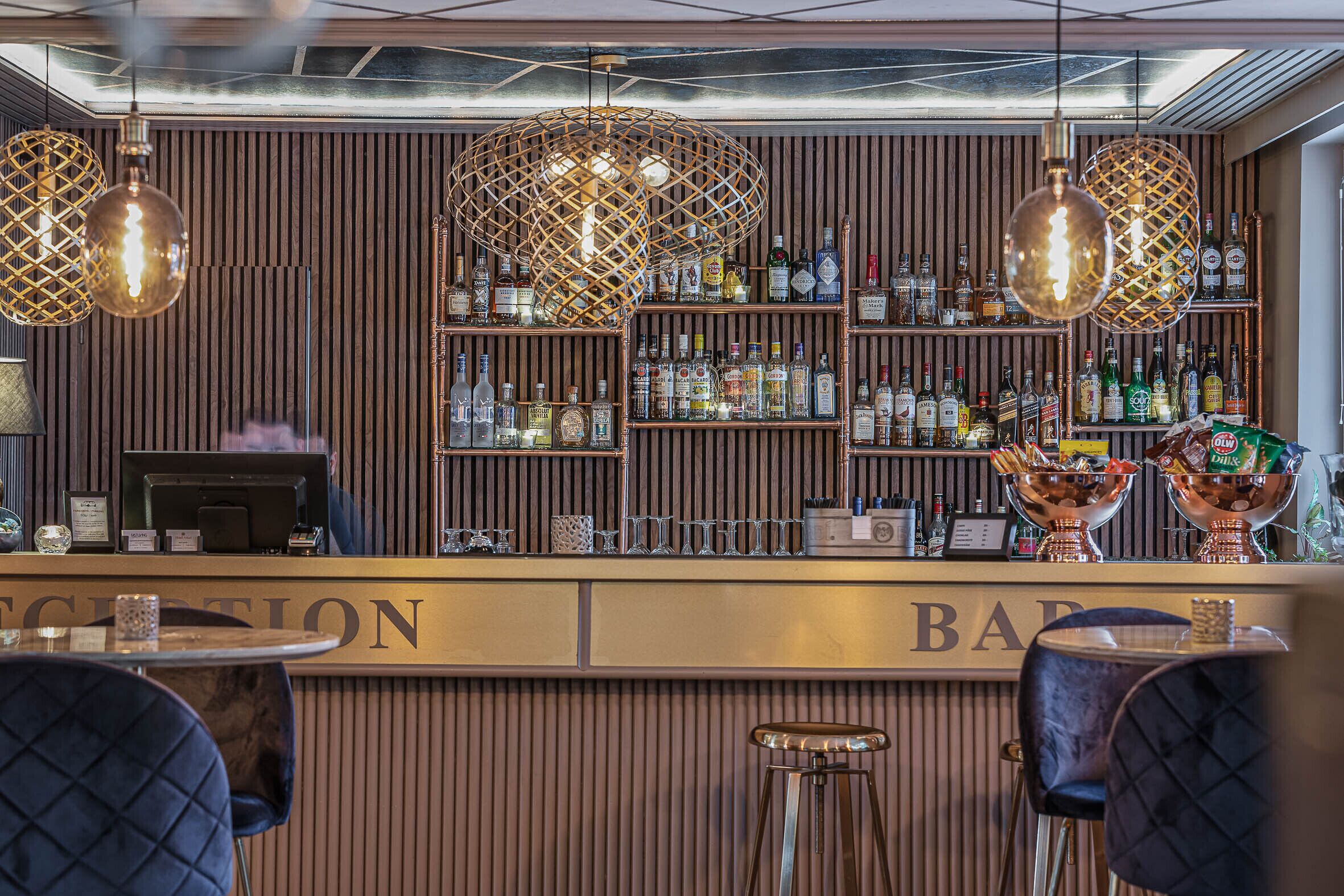 A bar area with a reception desk, wooden paneling, and hanging light fixtures.