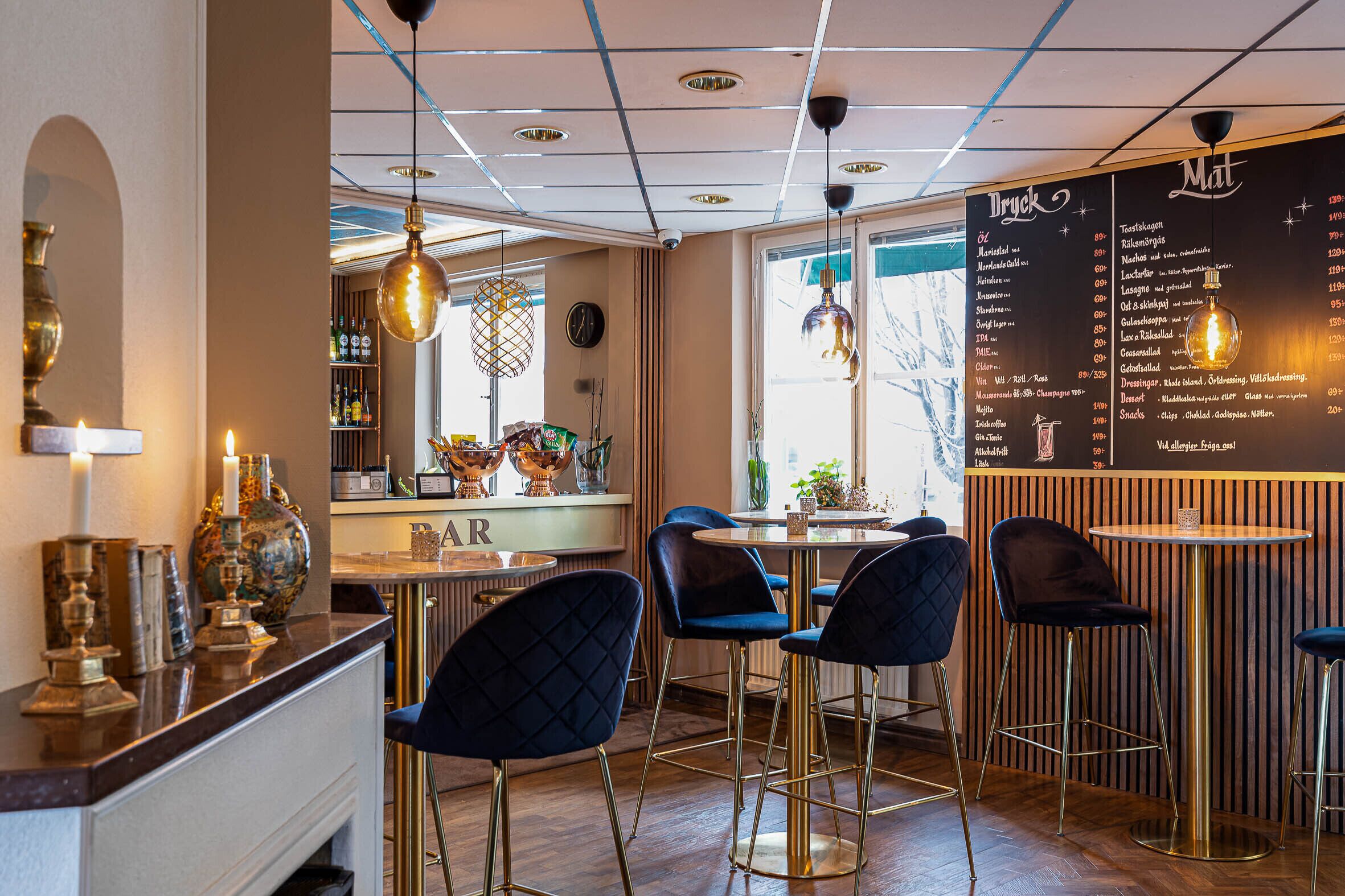 Zona de bar con taburetes altos, un tablero de menú e iluminación colgante.