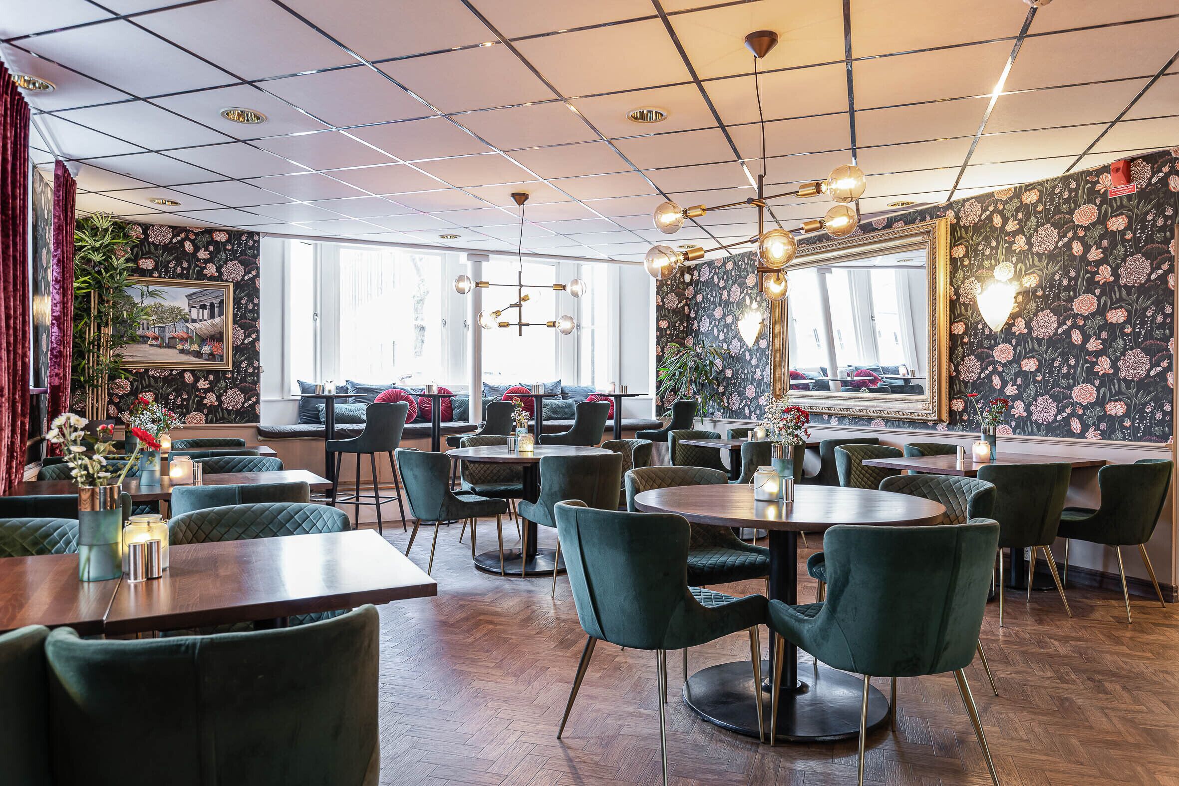 Un restaurant avec des chaises à revêtement vert, des tables en bois et un papier peint à motifs floraux.